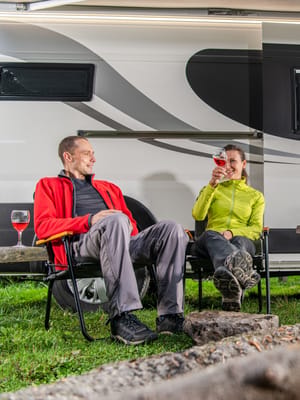 a couple boondocking without hookups in their rv in the woods near a campfire drinking wine